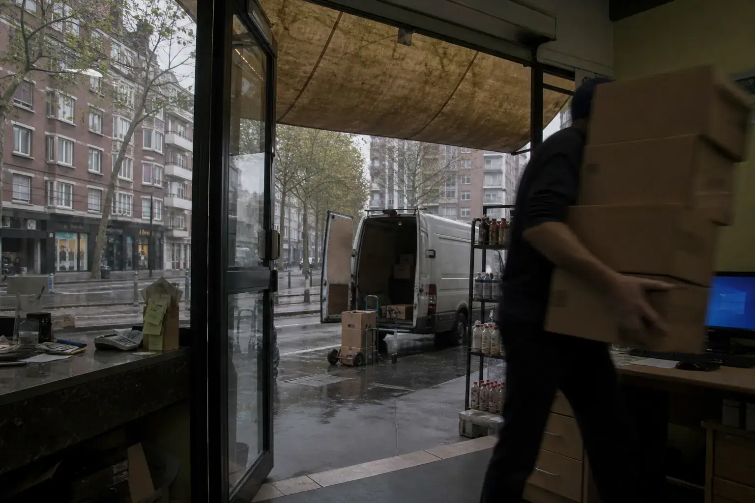 Commerce de proximité sur une avenue de banlieue lyonnaise, cartons portés du comptoir vers l’arrière-boutique