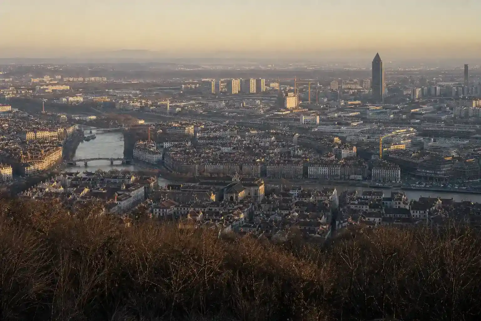 Vue de l’agglomération lyonnaise depuis une colline : cœur ancien, tours du quartier d’affaires, zones d’activité et monts au loin